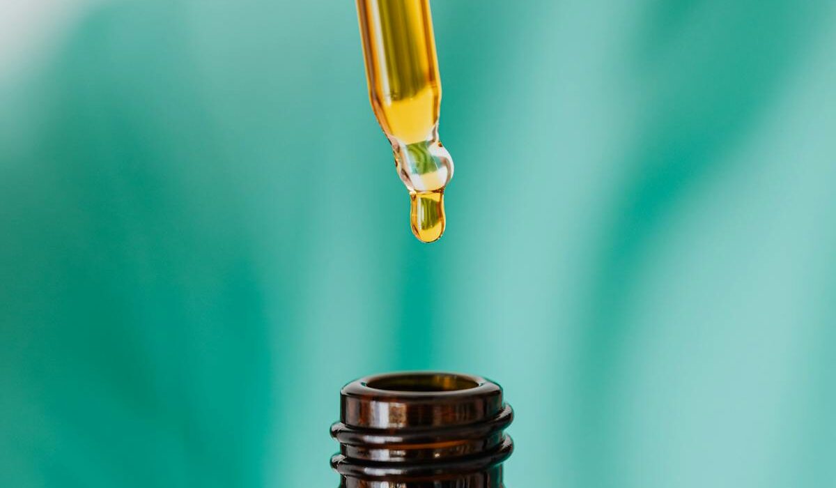 castor oil being poured from dropper into amber glass bottle for home castor oil packs