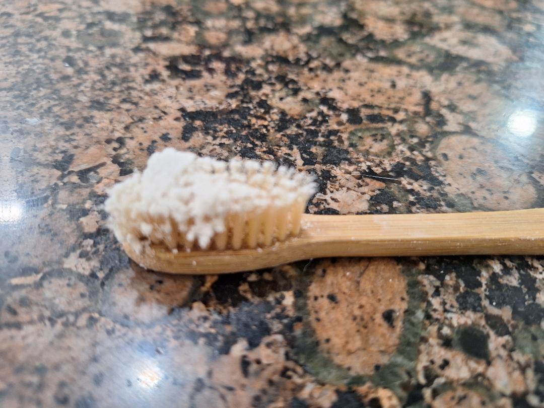 Bamboo toothbrush with pearl powder toothpaste clumped on the bristles, ready to use
