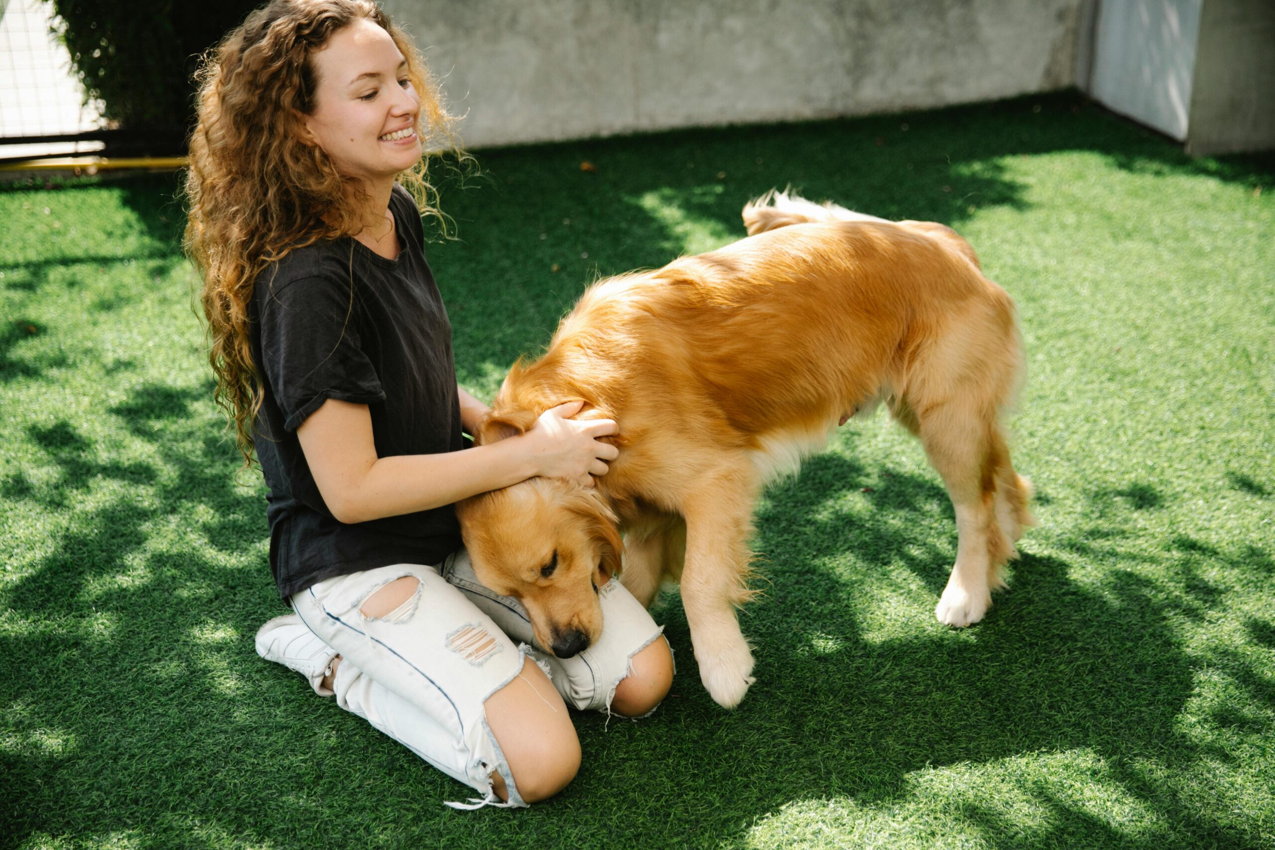 Woman smiling and petting her dog outdoors on a sunny day while checking its coat