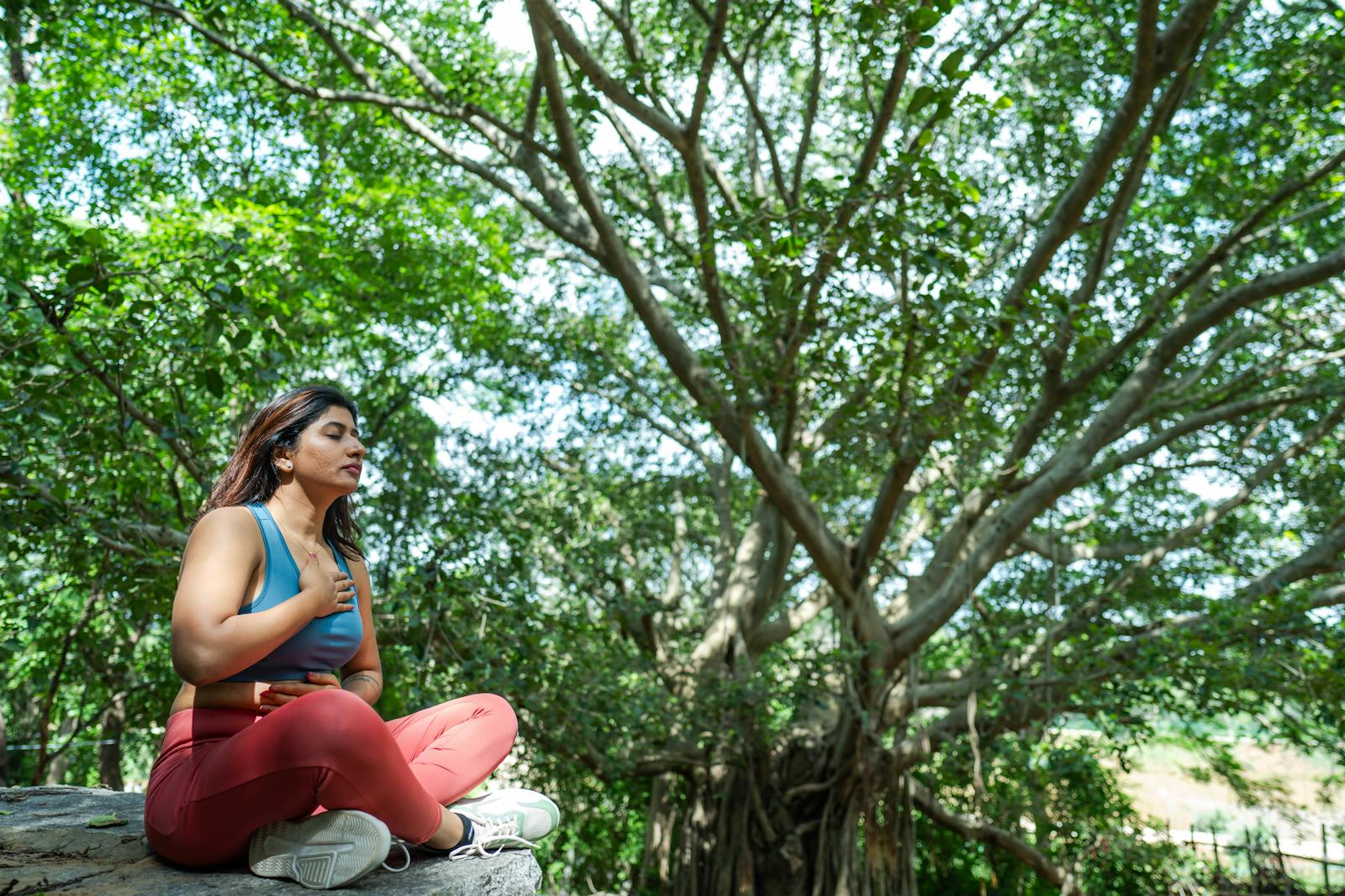 Woman meditating outdoors under a tree using box breathing for stress