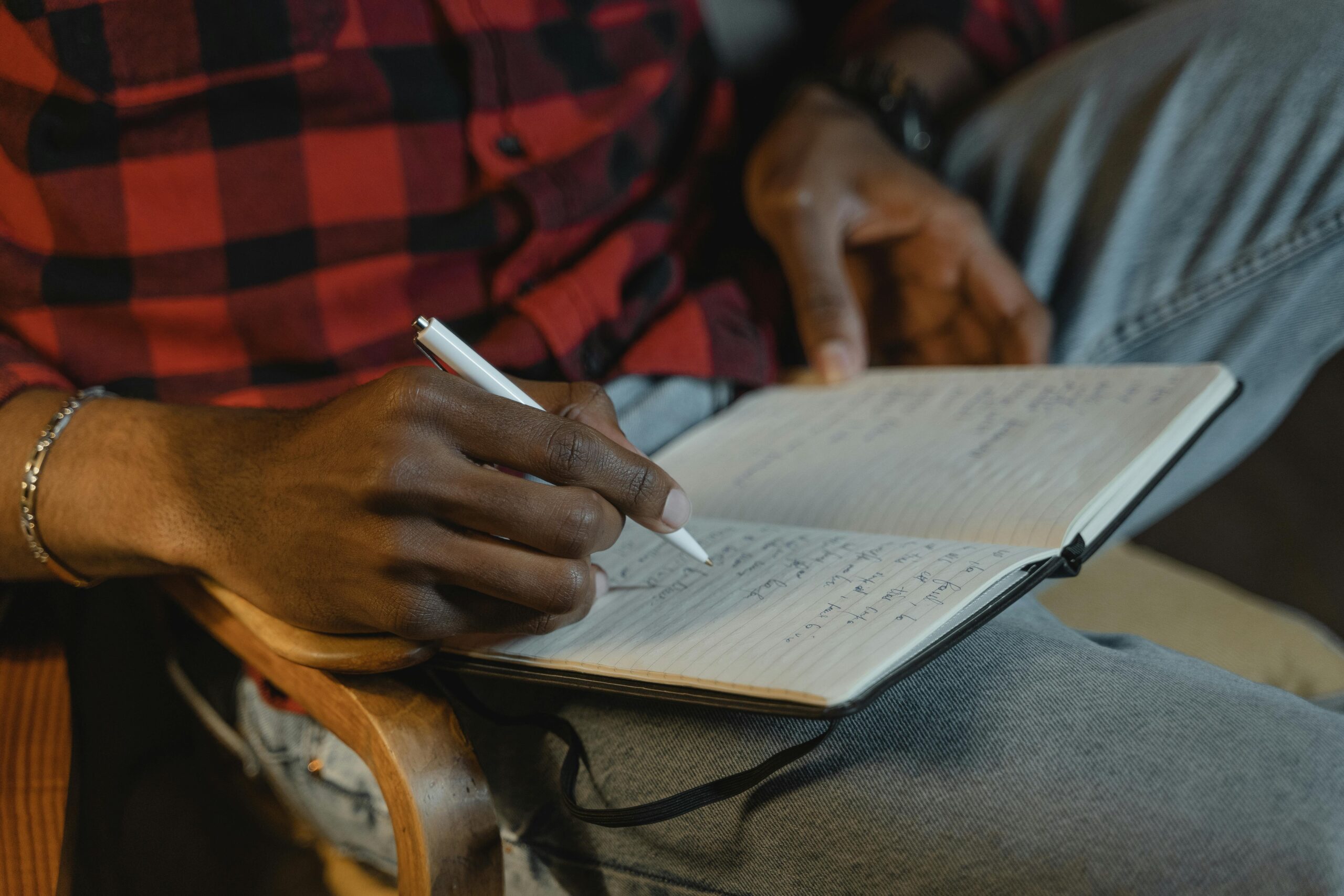 Close up of a person writing morning pages with a pen on open notebook pages