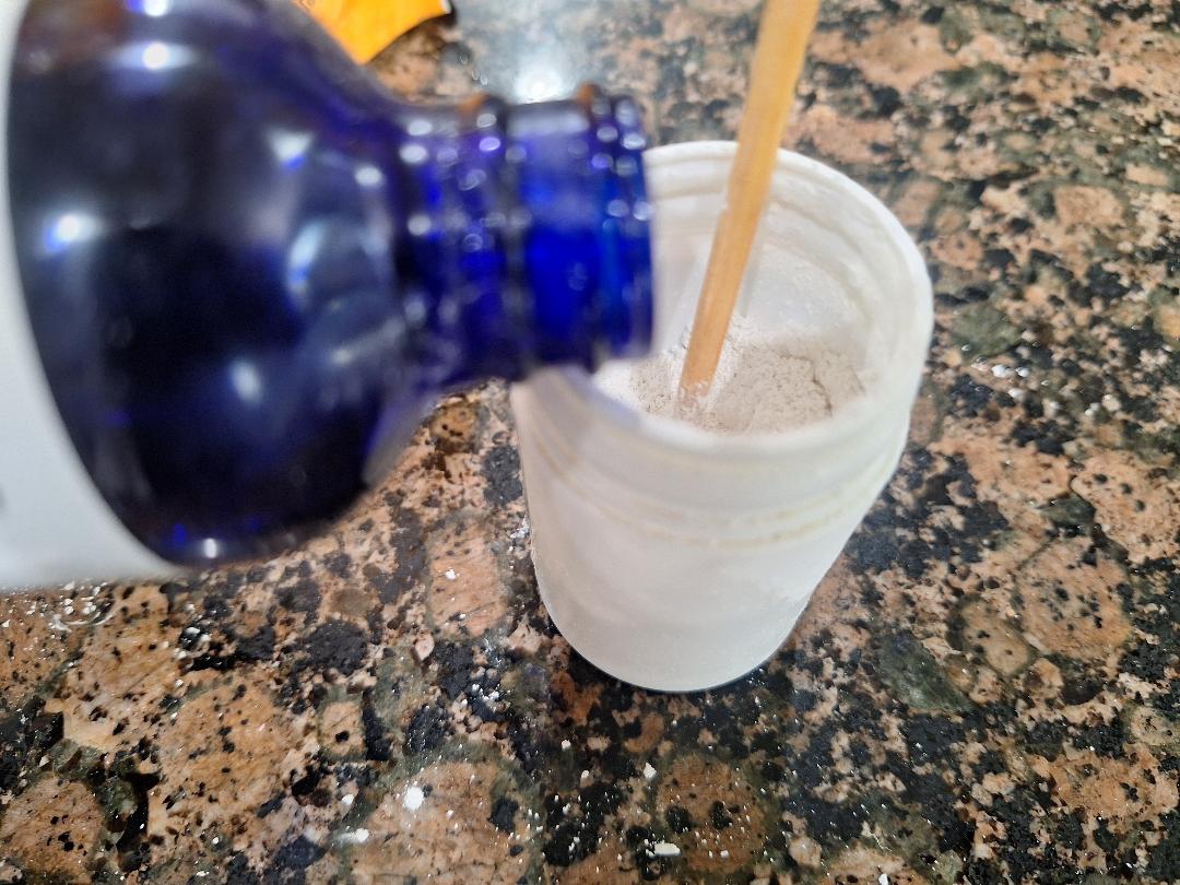 Pouring peppermint essential oil into the pearl powder and baking soda mix to finish the DIY toothpaste recipe