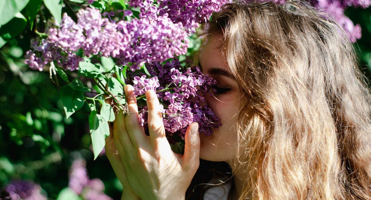 A woman smelling lilac flowers outdoors during spring allergy season.