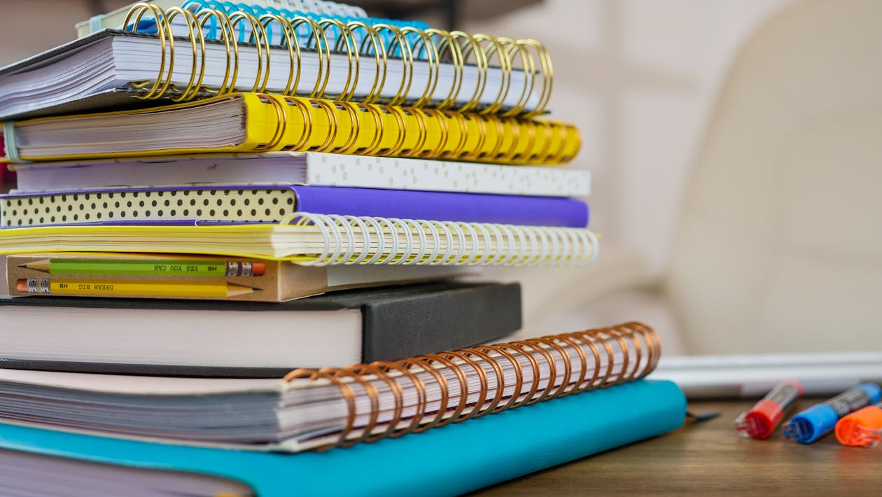 stack of journals and notebooks on wooden desk with pen for spring journaling practice