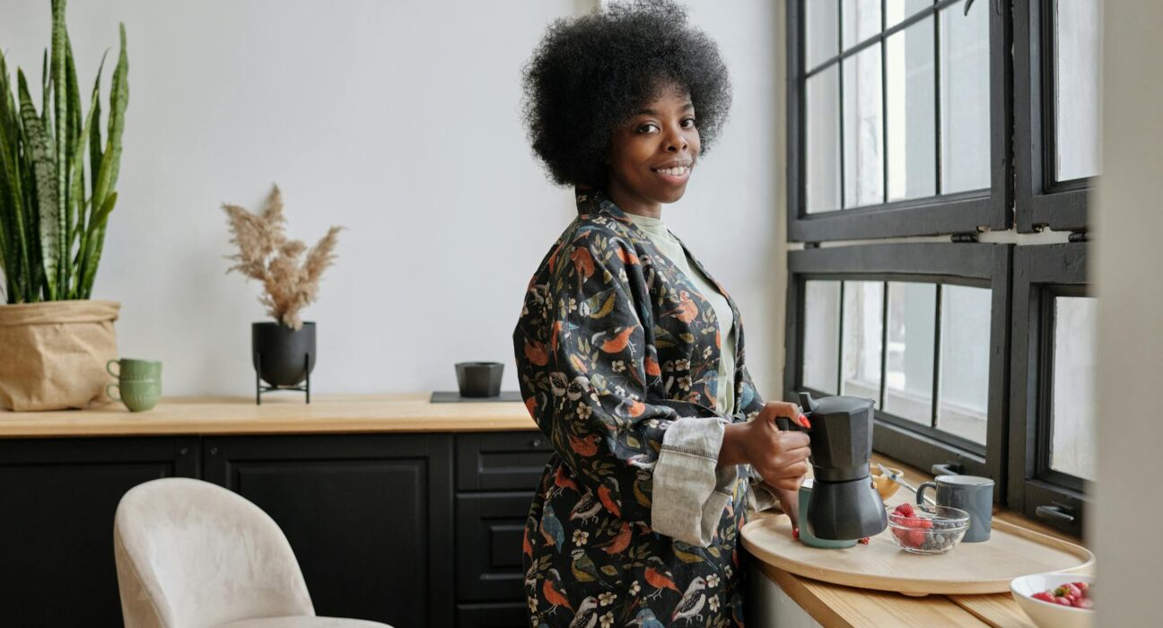 Woman in her forties holding a mug of dandelion root tea by a bright kitchen window in the morning