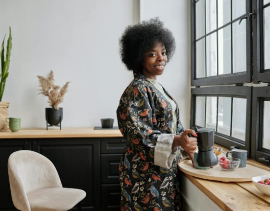 Woman in her forties holding a mug of dandelion root tea by a bright kitchen window in the morning