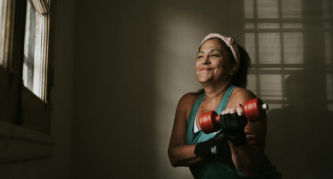 Woman in her forties lifting a moderate dumbbell in a bright home gym in the morning