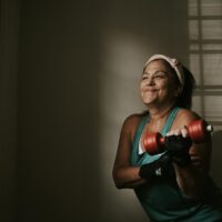 Woman in her forties lifting a moderate dumbbell in a bright home gym in the morning