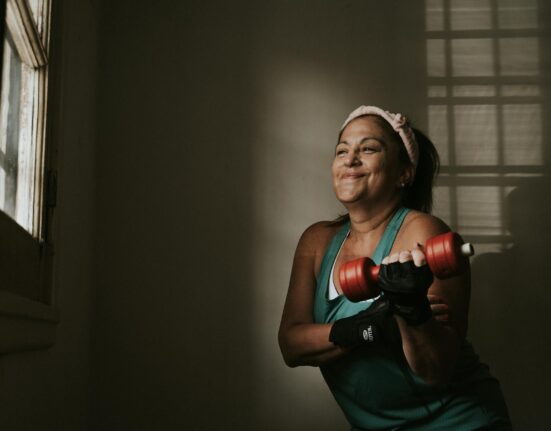 Woman in her forties lifting a moderate dumbbell in a bright home gym in the morning