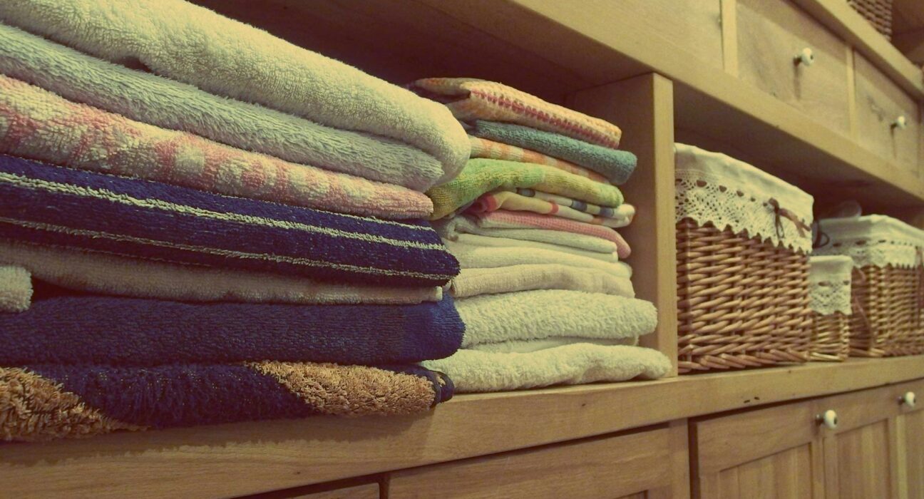 Stacked white cotton towels beside a non-toxic laundry detergent bottle on a clean wooden laundry room counter