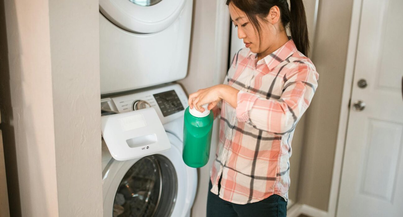 Three laundry soap formats — powder in glass jar, liquid in bottle, sheets in cardboard envelope — compared on a wooden counter