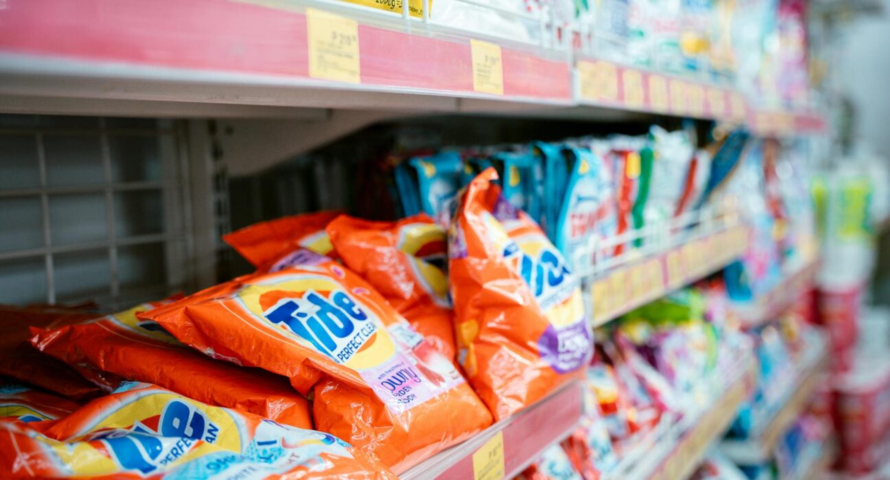 Row of mainstream laundry detergent bottles on a supermarket shelf with ingredient labels in focus