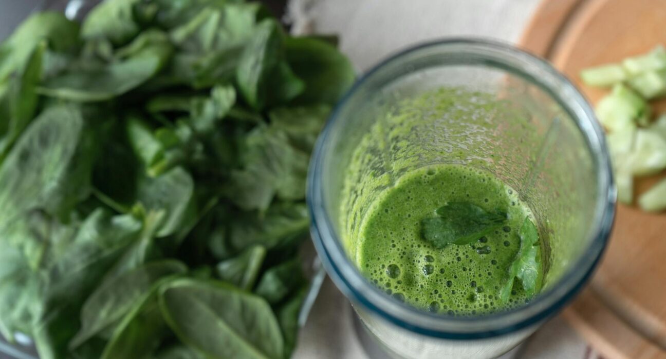 Heavy metal detox smoothie in a glass with cilantro garnish beside chlorella powder and berries