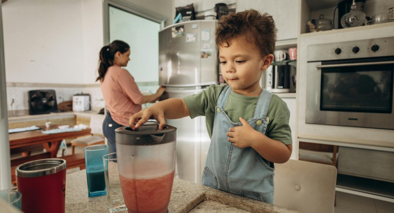 Young child drinking a green detox smoothie at the kitchen table with a parent