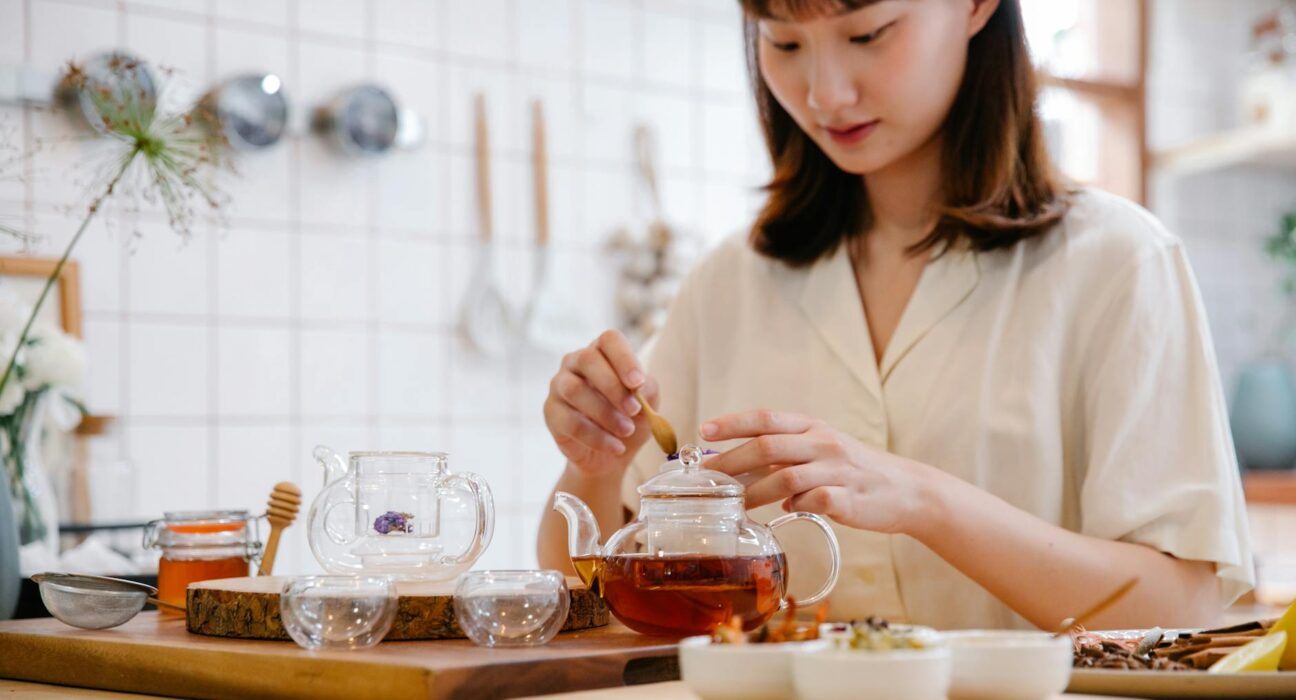 Woman drinking herbal tea in a bright kitchen looking calmer after anxiety