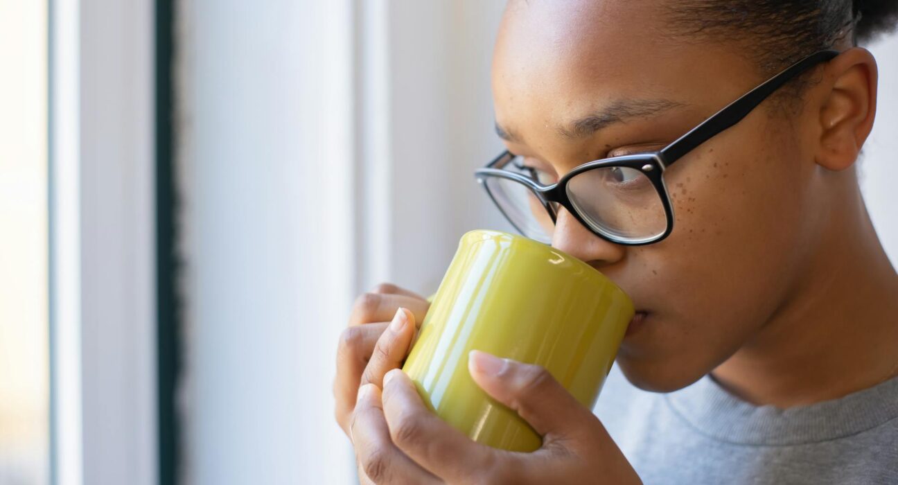 Woman with brain fog looking out a sunny window holding a steaming mug