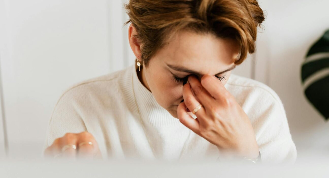 Woman gently rubbing tired eyes by morning kitchen window