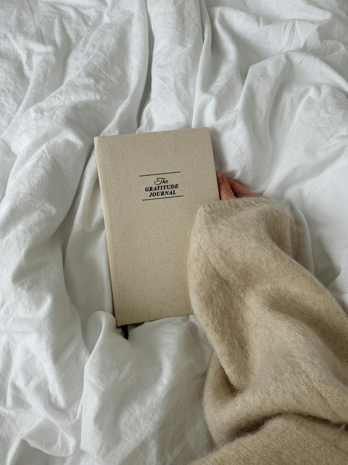 A hand holding a gratitude journal on a soft bed during evening reflection