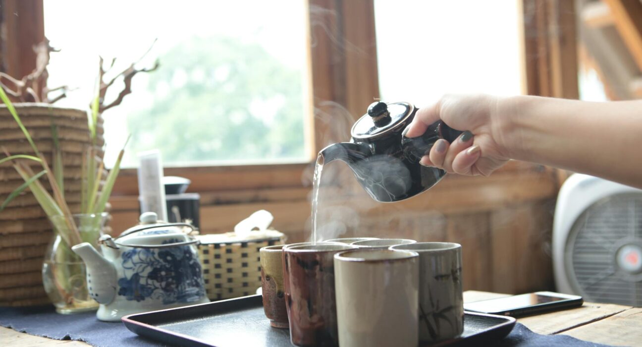 Steaming cup of herbal sinus tea with fresh ginger and turmeric on a wooden tray