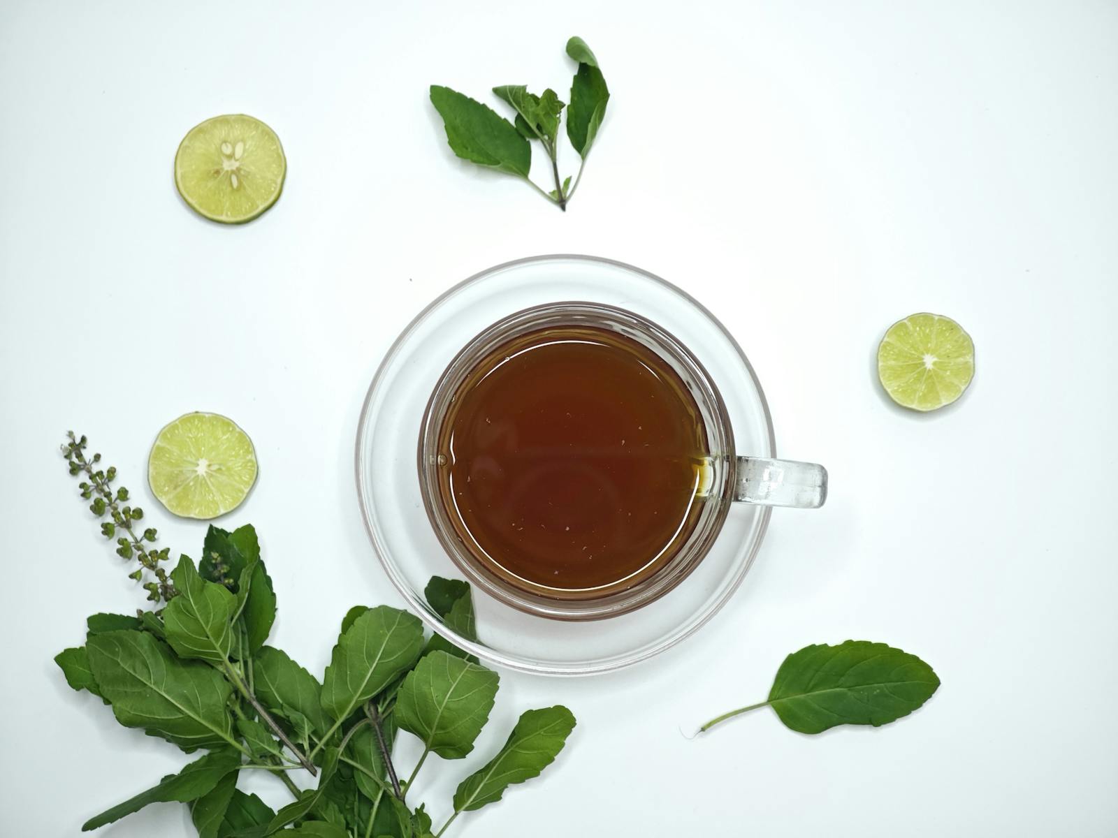 Holy basil tea benefits in a glass cup with fresh herbs and lime