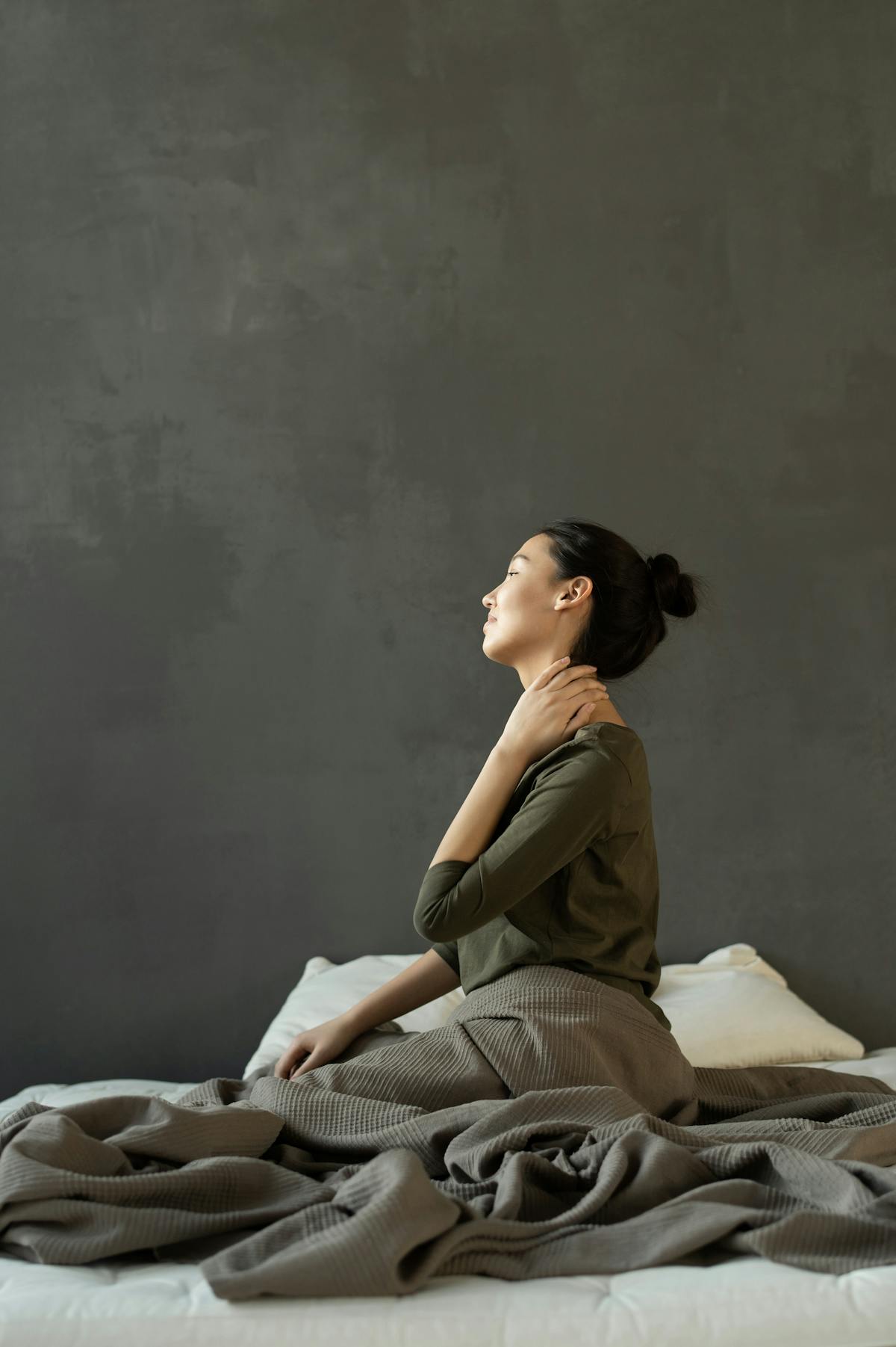 Woman softly touching thyroid area at side of bed soft lighting