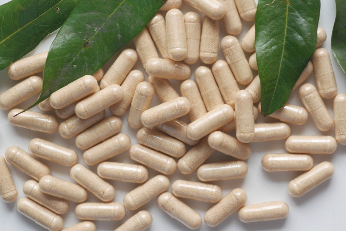 Bowl of mucuna pruriens herbal capsules and seeds on a wooden table