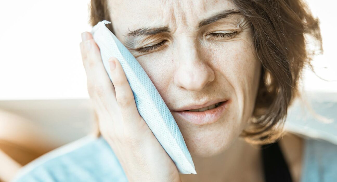 Woman gently holding cold compress to her cheek to ease combined sinus pressure and tooth pain