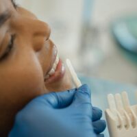 Smiling woman in dental chair holding a tooth shade guide to plan teeth whitening