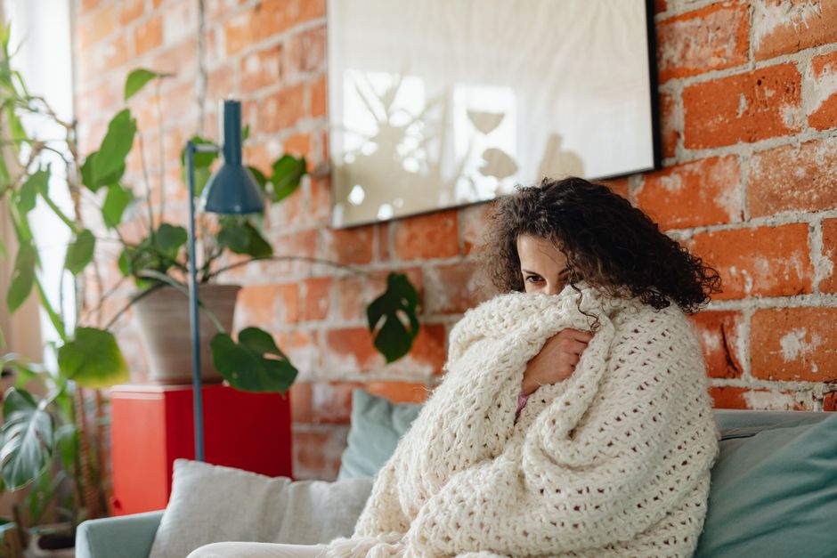 Adult woman wrapped in a cream blanket on a couch, demonstrating adult self-soothing techniques