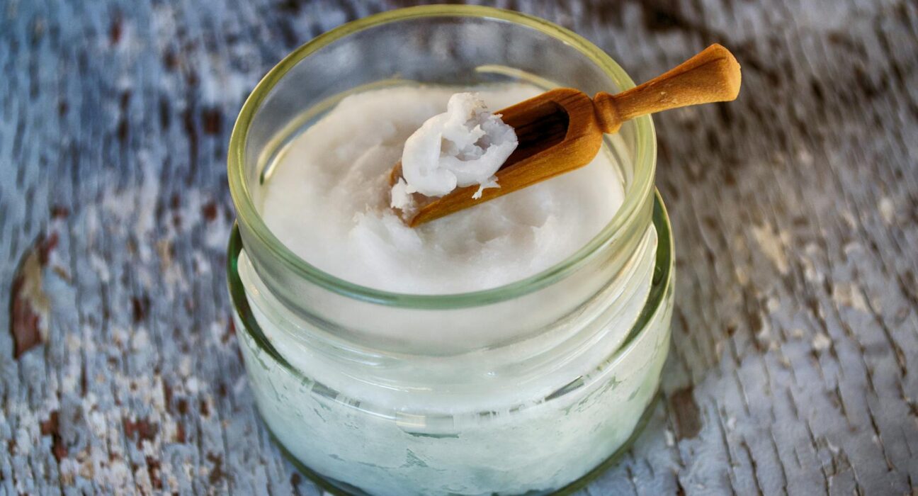 Organic coconut oil in glass jar with wooden spoon, the foundation of homemade coconut oil toothpaste