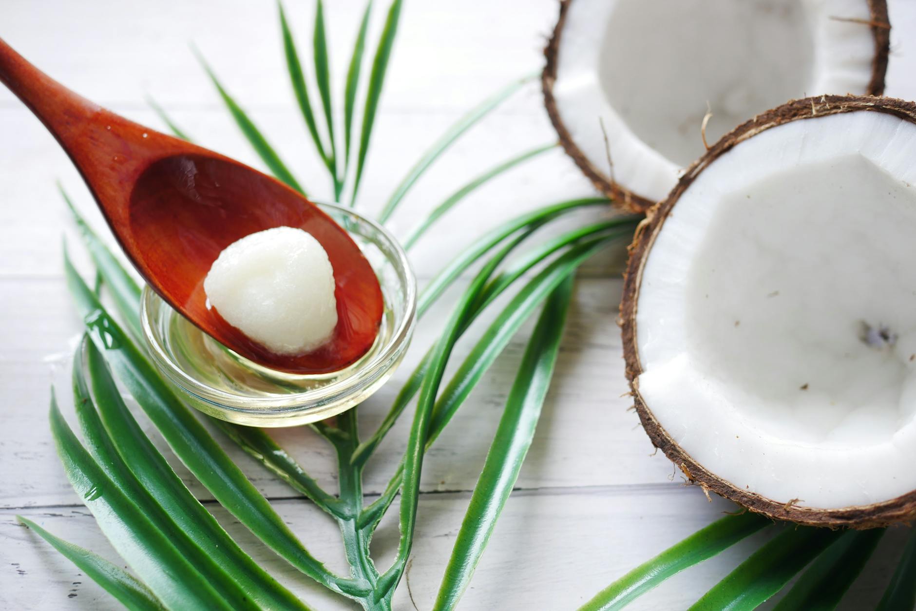 Close-up of organic coconut oil on a wooden spoon beside fresh coconut